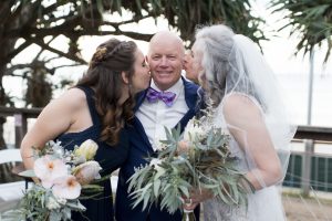 Groom enjoying a kiss from wife and daughter