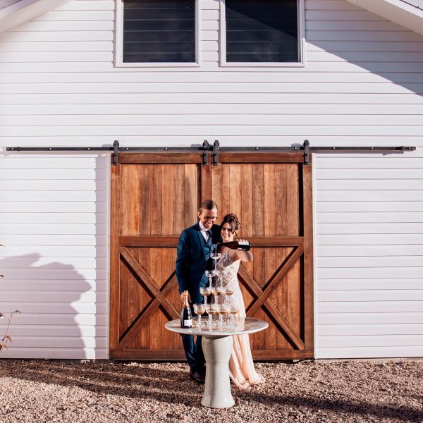 Newlyweds and a champagne tower at Aurora House, a Byron Bay hinterland wedding venue. They are in front of a barn door.