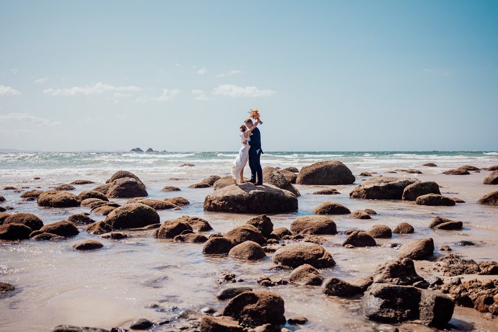 Bride and groom sharing first kiss on a rock at wategos beach byron bay