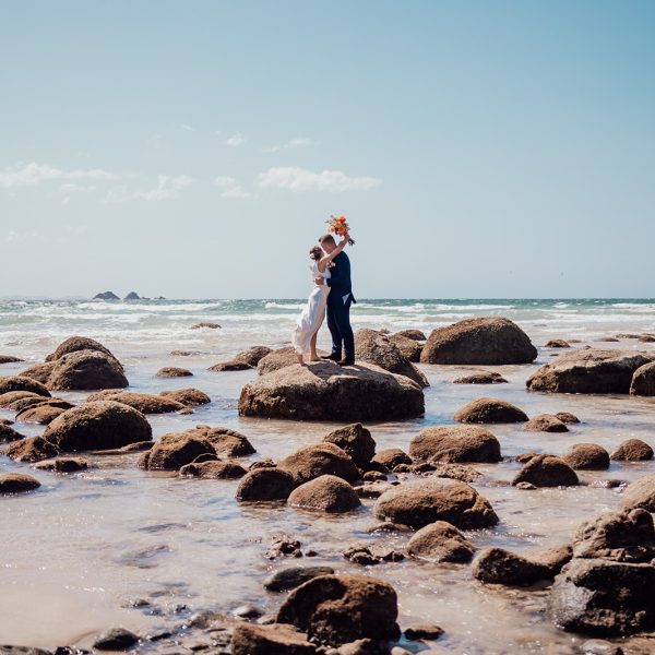 Bride and groom sharing first kiss on a rock at wategos beach byron bay